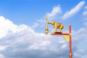 poste de lámpara eléctrica de elefante dorado en el camino de un parque contra el cielo azul. linterna general en las calles de tailandia. postes de luz rojos y dorados hay una estatua de elefante en la parte superior. foto