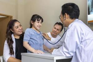 Asian doctor is diagnosis young girl using stethoscope for lung checkup and side effect on coronavirus with parent and family in her appointment in hospital concept photo