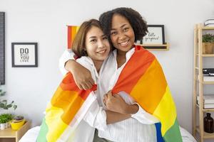 pareja de matrimonios del mismo sexo de diferentes razas sosteniendo la bandera del arco iris lgbtq para el mes del orgullo para promover la igualdad y las diferencias de homosexualidad y discriminación foto