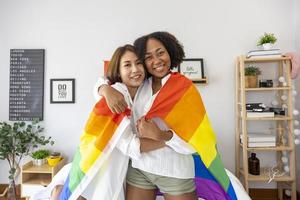 pareja de matrimonios del mismo sexo de diferentes razas sosteniendo la bandera del arco iris lgbtq para el mes del orgullo para promover la igualdad y las diferencias de homosexualidad y discriminación foto
