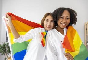 pareja de matrimonios del mismo sexo de razas diferentes que sostienen la bandera del arco iris lgbtq para el mes del orgullo para promover la igualdad y las diferencias del concepto de homosexualidad y discriminación foto