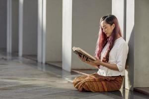 Asian buddhist woman is reading Sanskrit ancient Tripitaka book of Lord Buddha dhamma teaching while sitting in temple to chant and worship in the monastery photo