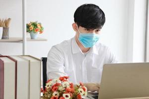 Male employee wearing medical facial mask working alone as of social distancing policy in the business office during new normal change lifestyle after coronavirus or post covid-19 outbreak situation photo