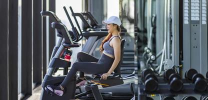 mujer asiática haciendo ejercicio usando una máquina de ciclismo para entrenamiento cardiovascular dentro del gimnasio para un estilo de vida saludable con espacio para copiar foto