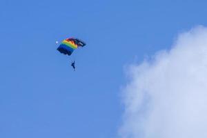 el piloto vuela en parapente con deslizamiento arcoíris para promover lgbtq en la igualdad de género en el deporte extremo con un cielo azul brillante y una nube blanca y esponjosa foto