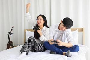 Asian couple having fun playing video game console together in bed with copy space for E-Sports and online gamer concept photo