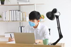 Male employee wearing medical facial mask working alone as of social distancing policy in the business office during new normal change lifestyle after coronavirus or post covid-19 outbreak situation photo