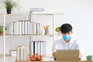 Male employee wearing medical facial mask working alone as of social distancing policy in the business office during new normal change lifestyle after coronavirus or post covid-19 outbreak situation photo
