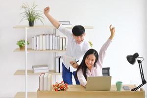 Happy Asian couple celebrating their new high sale after using computer laptop for online auction while working from home for new normal policy with copy space photo