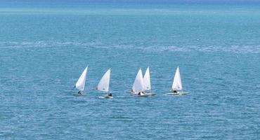 grupo de veleros optimistas de bote blanco navegando en mar abierto con un color azul turquesa soleado para actividades de verano y vacaciones foto