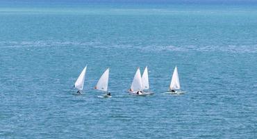 Group of white dinghy optimist sailboat sailing in the open sea with sunny blue turquoise color for summer activities and vacation photo