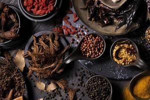 varios tipos de especias secas de sabor terroso oriental sobre una mesa de madera oscura como cúrcuma, pimienta negra, copos de chile, hojas de laurel, para uso medicinal y herbal en la curación y el uso de la cocina foto