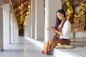 mujer budista asiática está leyendo sánscrito antiguo manuscrito de hoja de palma de tripitaka el señor buddha dhamma enseñando mientras está sentada en el templo el día sagrado de la luna llena para cantar y adorar en el monasterio foto