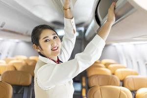 Asian female flight attendant closing the overhead luggage compartment lid for carry on baggage after passengers are seated and prepare to take off photo