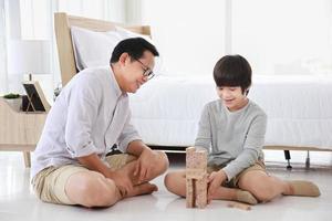 Asian father and son concentrate on playing wooden block together at home for edutainment concept photo