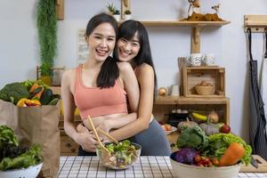 Asian couple of same sex marriage hugging each other while cooking healthy salad together in kitchen during pride month to promote equality and differences of homosexual and discrimination concept photo