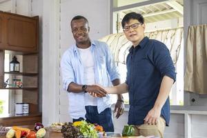 amigos asiáticos y africanos se dan la mano en casa mientras se ayudan mutuamente a cocinar verduras orgánicas para el concepto de preparación de ensaladas y comidas foto