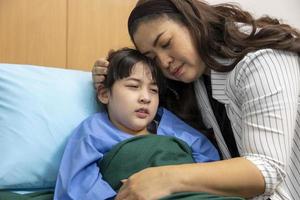 una niña asiática está llorando mientras recibe tratamiento para su enfermedad en el hospital con su madre apoyándola para calmarla foto