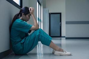 Medical nurse is sitting down on floor in frustration and grief after failure of patient body condition