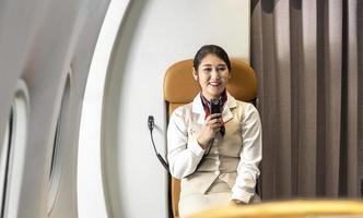 el asistente de vuelo asiático saluda al pasajero para darle la bienvenida a bordo del vuelo e informa la actitud, el clima y la ruta al aeropuerto de destino foto