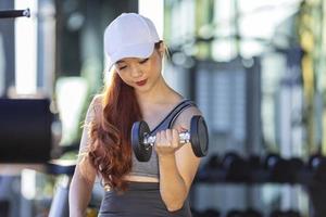 mujer asiática en ropa deportiva haciendo levantamiento de pesas para ganar músculo bíceps mientras entrena en el gimnasio con espacio para copiar foto