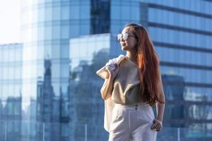 Luxury young Asian CEO woman entrepreneur standing on the rooftop looking to the sun with skyscraper and cityscape on the background