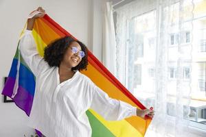 African American girl holding LGBTQ rainbow flag in her bed room for coming out of the closet and pride month celebration to promote sexual diversity and equality in homosexual orientation