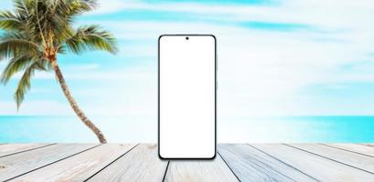 Phone mockup on wooden table with beach, palm and sea in background. Summer travel promotion concept photo