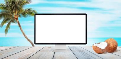 Computer display mockup on wooden table. Beach, palm and sea in background. Coconuts beside. Isolated white display for summer travel promotion photo