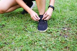 la persona o el atleta se atan un zapato preparándose para correr o hacer ejercicios en el césped del parque. para una buena salud, pérdida de peso, buena forma. foto