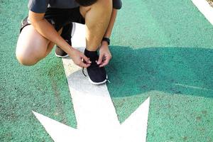 Person or athlete tie a shoe preparing getting ready for run or exercises on the green running ground in the park. For good health, loss weight, good shape. photo