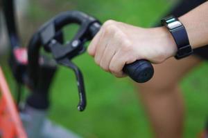 imagen de enfoque de la mano que sostiene el manillar de la bicicleta y la muñeca tiene un reloj inteligente en el parque. concepto de buena salud, pérdida de peso, buena forma. foto