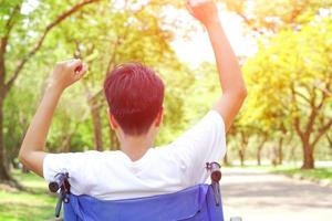 pacientes o discapacitados levantaron la mano con alegría. sentado en una silla de ruedas y mirando hacia adelante con esperanza. concepto médico y de salud. foto