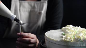 chef señora haciendo rosas de crema para la decoración de pasteles mientras hace panadería casera sobre fondo negro