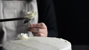 Küchenchefin, die Rosen aus Sahne für die Dekoration von Kuchen herstellt, während sie hausgemachte Backwaren auf schwarzem Hintergrund herstellt video