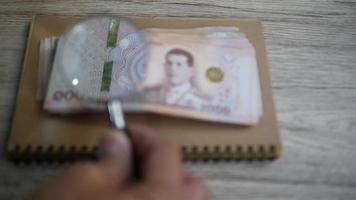 Business man is checking genuine Thai Banknote using magnifier