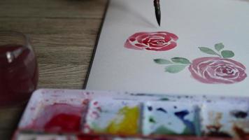 Woman paints the leaves of a rose with watercolors