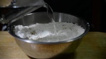 Chef pouring water into a dough bowl while preparing homemade bakery cake over black background video