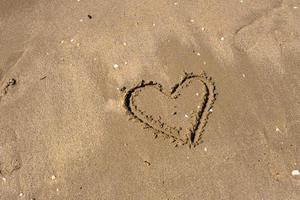 A drawing of a heart on a yellow sand at a beautiful seascape background. Horizontal composition. photo