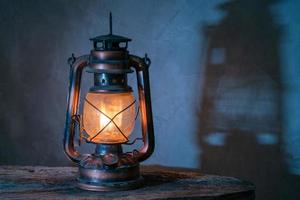 antique kerosene lamp with lights on the wooden floor in the gray old plaster background. soft focus. photo