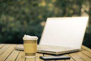 coffee cup paper with a Computer laptop in green nature background. Work remotely or from home. soft focus.shallow focus effect. photo