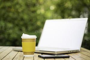 coffee cup paper with a Computer laptop in green nature background. Work remotely or from home. soft focus.shallow focus effect. photo