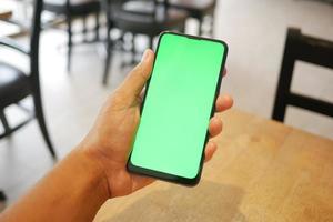 mano de hombre joven usando un teléfono inteligente con pantalla verde en el café foto