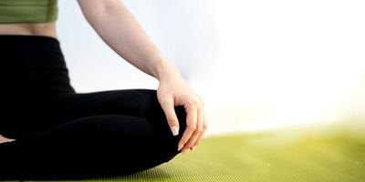 mujer practicando clases de yoga, respirando, meditando sentada en una alfombra de yoga verde, en el hogar. foto