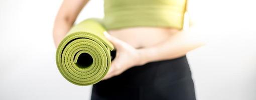 mano femenina sosteniendo una alfombra de yoga verde para preparar el ejercicio en la alfombra. foto