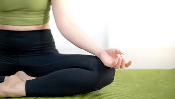 mujer practicando clases de yoga, respirando, meditando sentada en una alfombra de yoga verde, en el hogar. foto