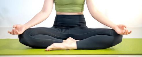 mujer practicando clases de yoga, respirando, meditando sentada en una alfombra de yoga verde, en el hogar. foto