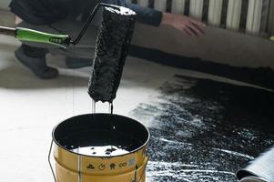 Applying hot resin to the floor for waterproofing, roller and bucket of resin. photo