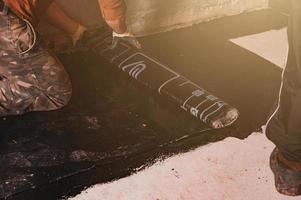 The worker untwists the roll of waterproofing and fastens it to the resin. photo