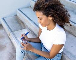 Hispanic female happily taking notes while sitting on the stairs photo